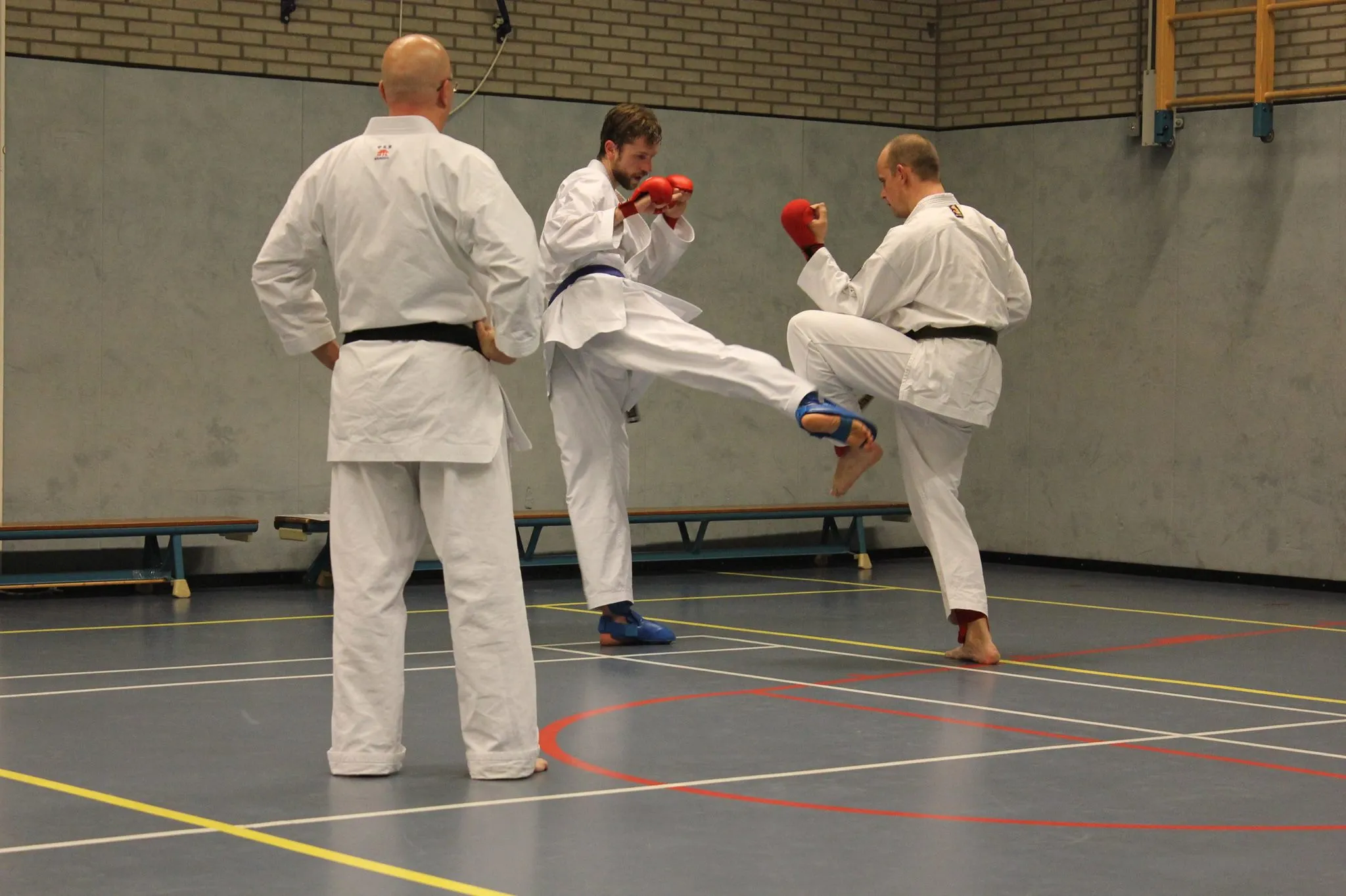 Twee karateka's met beschermers sparren tijdens kumite, met een trap naar het lichaam